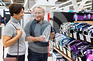 Older couple picking out new clothes iron to buy in electronics department of supermarket