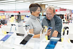Older couple picking out new phone to buy in electronics department of supermarket