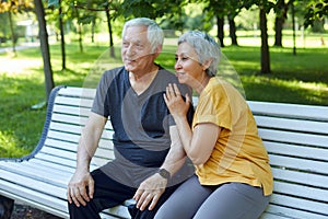 Older couple resting in park seated on bench enjoy talk