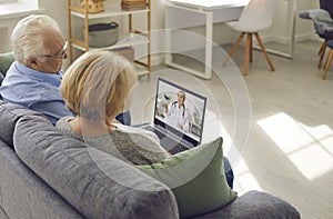 Older couple is sitting at home in the living room and talking to their family doctor via video link
