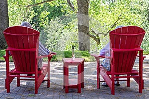Older couple sitting in red Muskoka chairs