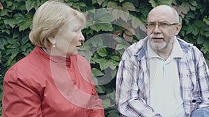 An older couple talks as they sit on a bench