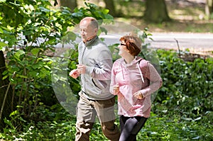 Older couple wearing sportswear and running in forest at mountain