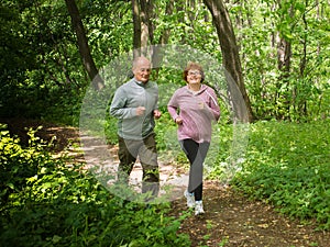 Older couple wearing sportswear and running in forest at mountain