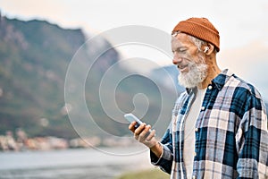 Older elder hipster man standing in nature park wearing earbud using phone.