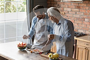 Older father and adult son cook in kitchen