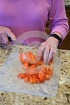 Elderly woman cuts tomatoes on counter