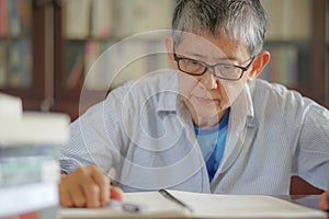 Older gray hair woman thoughtfully handwriting testament. Senior woman sitting at desk
