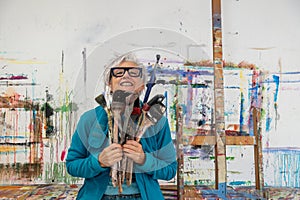 older gray haired mature happy smiling artist woman proud artist, in her fifties with grey hair and glasses and big paintbrushes,