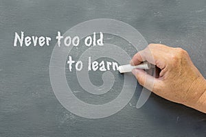 Older hand writes on a chalkboard: Never too old to learn