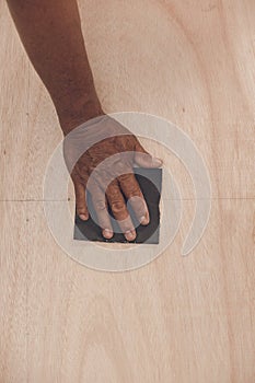 An older handyman using a piece of sandpaper to smoothen out the surface of a sheet of plywood prior to painting. photo