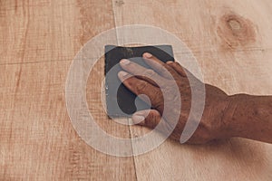 An older handyman using a piece of sandpaper to smoothen out the surface of a sheet of plywood prior to painting. photo