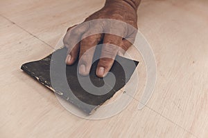 An older handyman using a piece of sandpaper to smoothen out the surface of a sheet of plywood prior to painting. photo