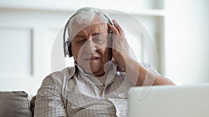 Older happy man wearing wireless headphones, enjoying favorite music.