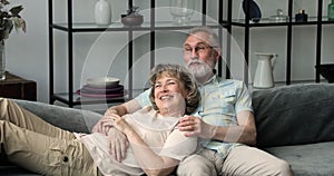 Older husband sit on sofa hug serene wife dream together