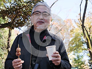 An older Japanese man eating dango and drinking coffee