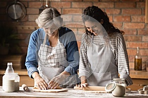 Older latin mother and daughter in law kneading rolling dough