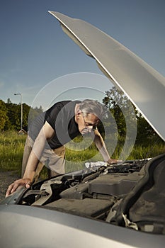 Older man alone on route checking unfunctional engine in late summer light