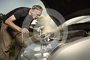 Older man alone on route checking unfunctional engine in late summer light