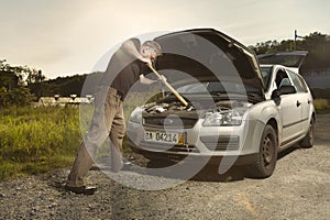 Older man alone on route checking unfunctional engine in late summer light