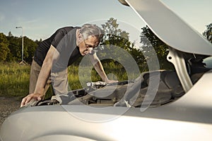Older man alone on route checking unfunctional engine in late summer light
