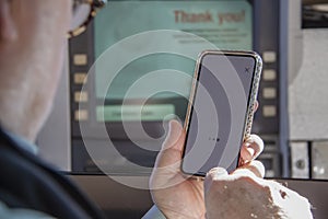 Older man attempting to use phone to complete a transaction at a drive up ATM machine - selective focus