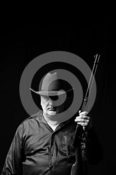 Older man in a cowboy hat with a gray beard holding a lever action rifle with a black background