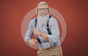 an older man in hipster clothes and glasses and long white beard listens to music and dance happily in the street focus on head