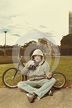 Older man in hooded shirt and mask relaxing with scooter in park