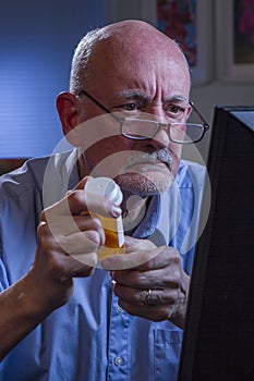 Older man looks concerned while refilling prescription online, vertical