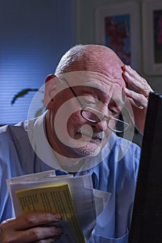 Older man looks stressed as he pays bills online, vertical