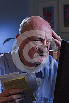 Older man looks worried as he pays bills online, vertical