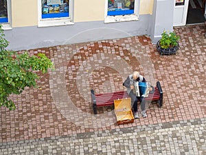 An older man playing the button accordion while sitting on a sidewalk bench