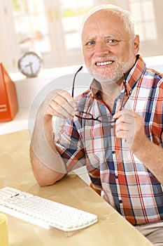 Older man putting on glasses at desk