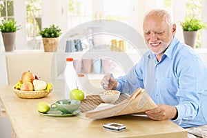 Older man reading newspaper in kitchen
