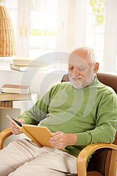 Older man relaxing at home, reading book photo