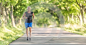 Older man runs uphill in the nature during a summer day keeping his fitness level high