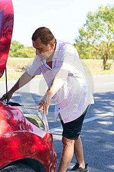 Older man searching for mechanical problem in a broken down car engine on the side of the road