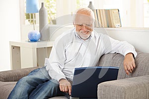 Older man smiling at computer screen at home photo