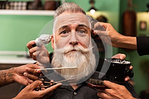An older man with a white beard is shaved, combed, hair cut by several hands of hairdressers and barbers. barbering tools