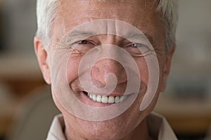Older man with wide toothy smile staring at camera, closeup