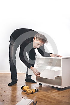 Older man working at home on kit of cabinet with laminated wooden drawers