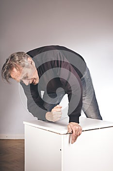 Older man working at home on kit of three wooden drawers on wheels