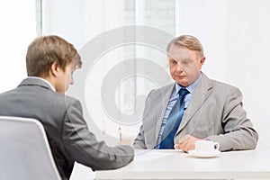 Older man and young man signing papers in office