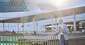 Older mature business man using smartphone standing in city outdoors.