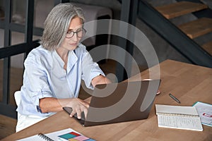 Older mature middle aged woman using laptop computer sitting at work desk.