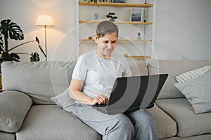 Older mature woman using wireless laptop apps browsing internet sit on sofa, smiling middle aged grandmother working