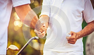 Older men stand on a golf course and talk. Handshaking