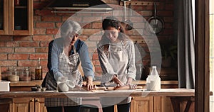 Older mother her adult daughter preparing dough together in kitchen