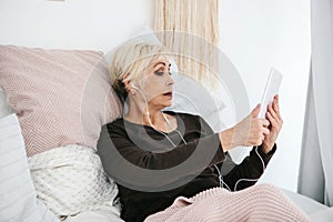 An older positive woman uses a tablet to watch videos, listen to music and chat with friends on social networks.